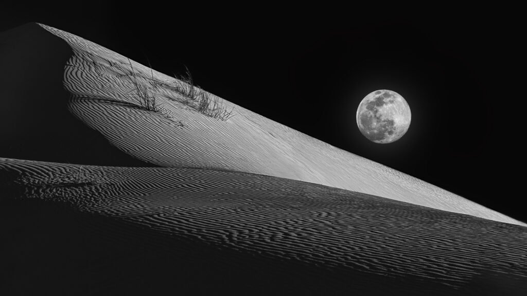 Composite photograph of sand dunes at Monahans Sandhills State Park in Texas, with a full moon added above the dunes for dramatic effect.