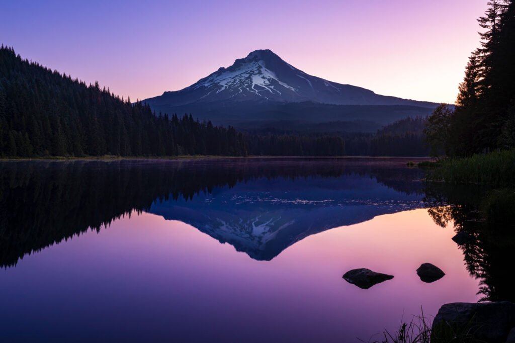 Mount Hood reflected in the calm waters of Trillium Lake at dawn, beneath a soft pink and purple sky.