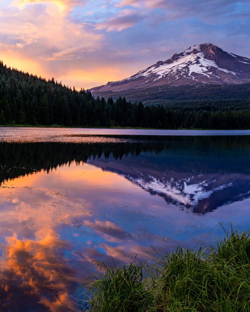 Mount Hood reflected in Trillium Lake at sunset, with warm pink and orange light in the sky and reflected across the water.