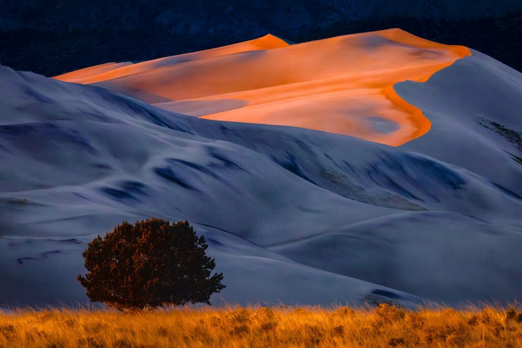 Sunset light across the dunes at Great Sand Dunes National Park in Colorado, with sunlit slopes glowing
orange-red and shaded dunes reflecting cool blue light