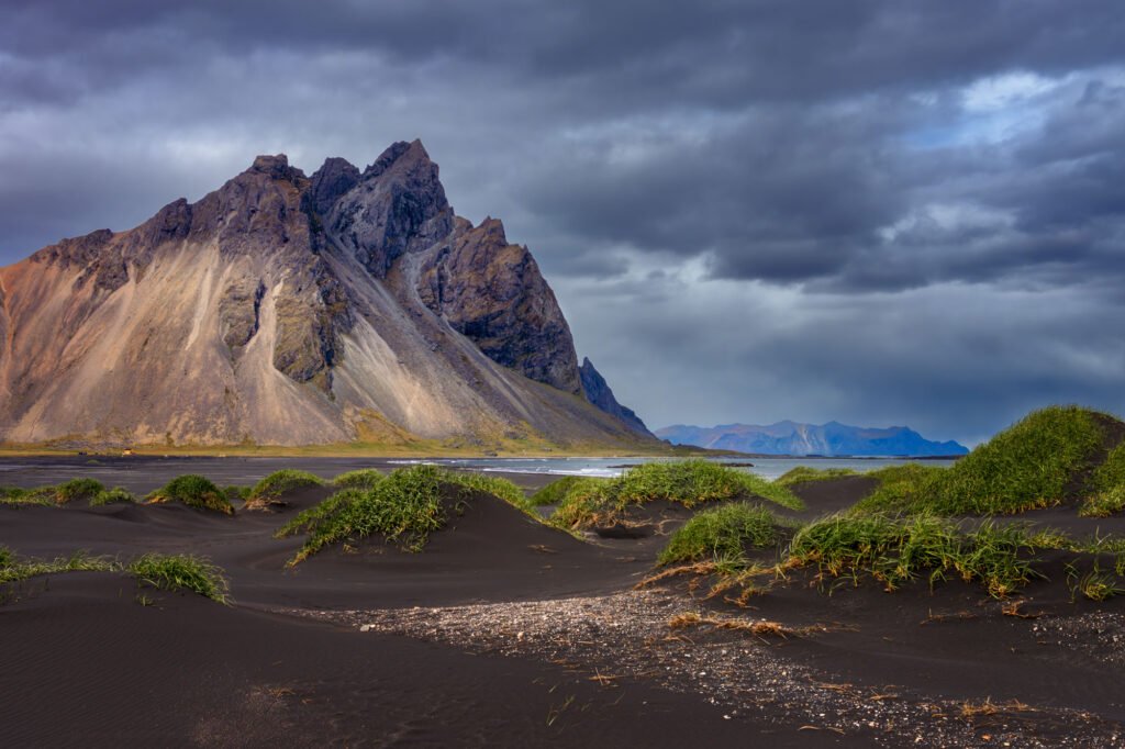 Vestrahorn rising above the black-sand dunes at Stokksnes, Iceland, beneath a dark and dramatic stormy sky.