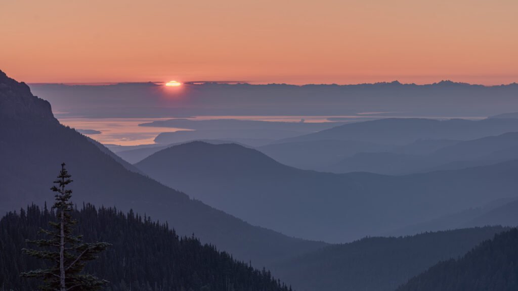 Sunrise at Hurricane Ridge in Olympic National Park, with the sun touching the eastern horizon and mist and haze separating multiple layers of mountain ridges.
